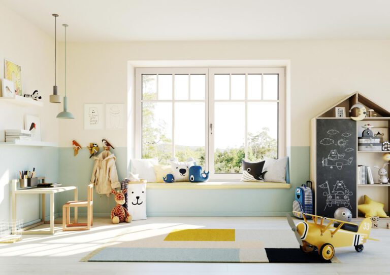 Das Foto zeigt ein modernes und helles Kinderzimmer mit einem großen Fenster in der Mitte. Vor dem Fenster befindet sich eine breite Fensterbank, auf der mehrere Kissen in Tierform und anderen freundlichen Designs liegen. Das Zimmer ist liebevoll und kindgerecht eingerichtet. Links steht ein kleiner Schreibtisch mit einem Stuhl, darauf stehen Stifte und Bücher. Daneben hängen an der Wand mehrere Garderobenhaken, an denen eine Jacke und ein Plüschtier angebracht sind. Auf dem Boden sitzen ein Stofftier in Giraffenform und ein Kissen mit Tiergesicht. Rechts steht ein Regal in Hausform, dessen Tür als Tafel genutzt wird und mit Kreide Bilder von einem Flugzeug und Tieren gezeichnet sind. Ein gelbes Spielzeugflugzeug steht vorn auf dem gemusterten Teppich. Das Zimmer wirkt freundlich und einladend, mit vielen liebevollen Details für Kinder. Das Tageslicht sorgt für eine helle und freundliche Atmosphäre.