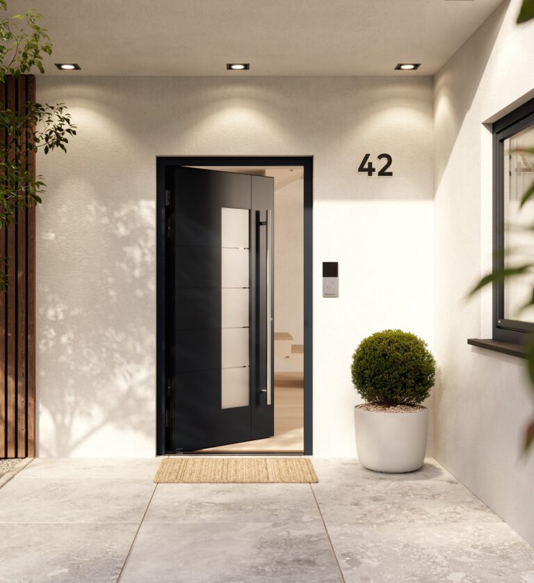 Moderner, überdachter Hauseingang mit geöffneter dunkelgrauer Haustür mit Glaseinsatz, Hausnummer 42, seitlicher Klingel- und Sprechanlage sowie rundem Buchsbaum im weißen Pflanzkübel auf einem hellen Steinboden