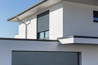 Modernes Einfamilienhaus in Weiß mit anthrazitgrauem Aufsatzrollladen am Obergeschossfenster und passendem Garagentor, vor strahlend blauem Himmel.